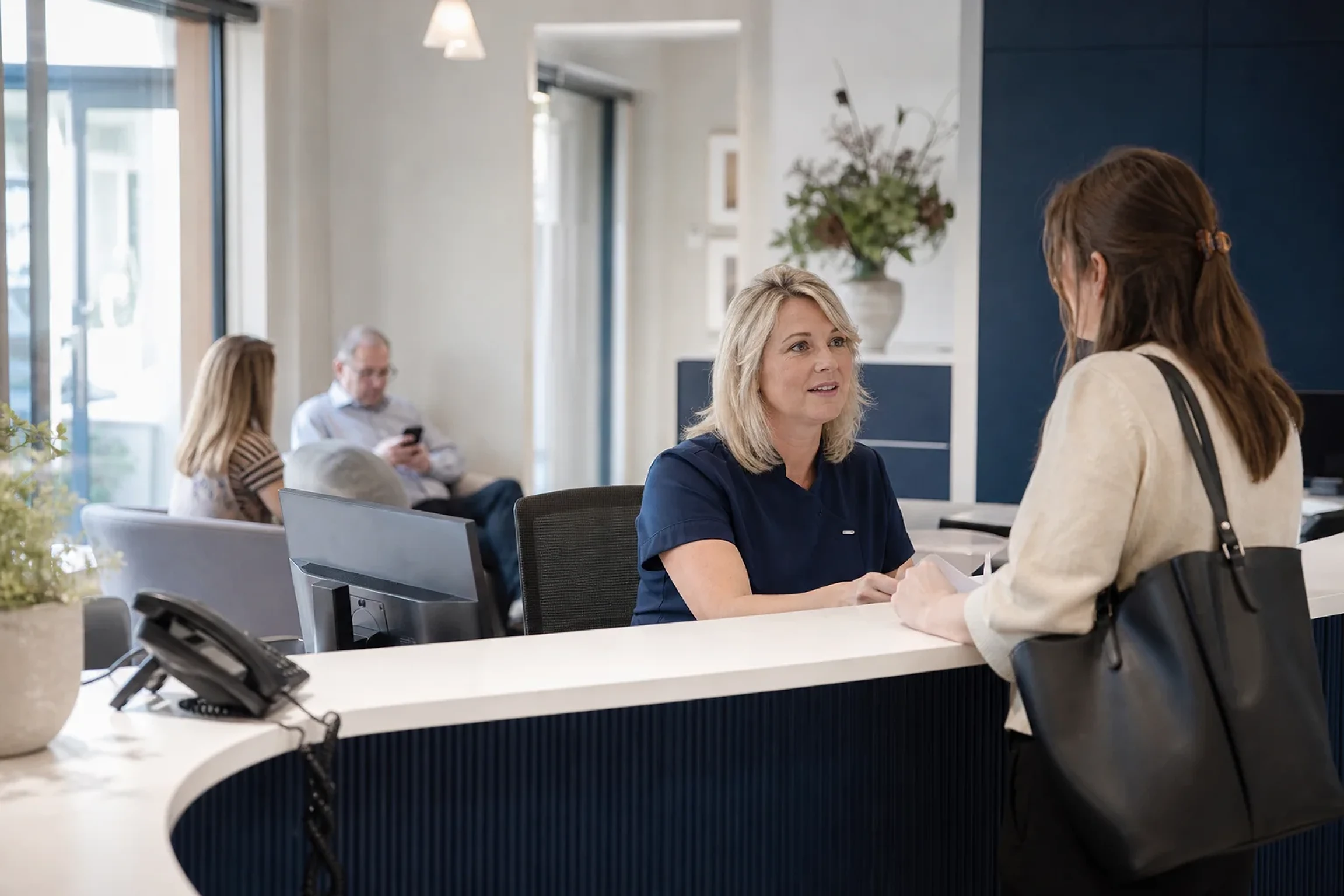 A receptionist helping a patient at a busy contemporary dental practice